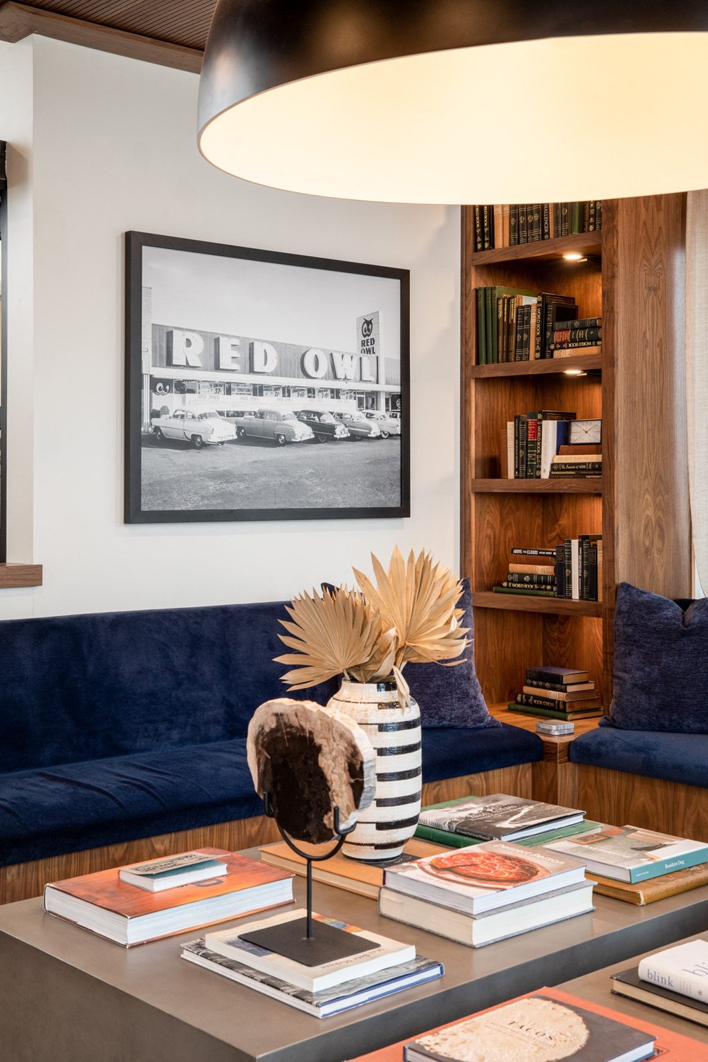 a living room with a blue couch and a coffee table with books and a vase with