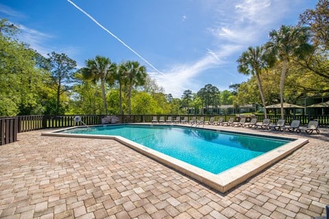 a swimming pool with chairs and trees in the background