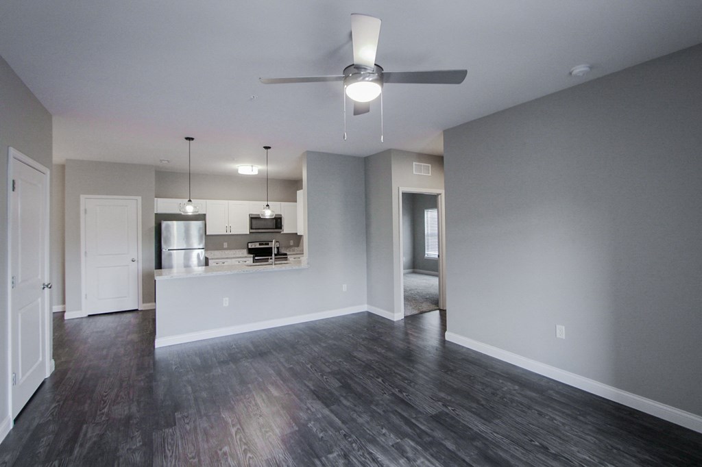 an empty living room with a ceiling fan and a kitchen