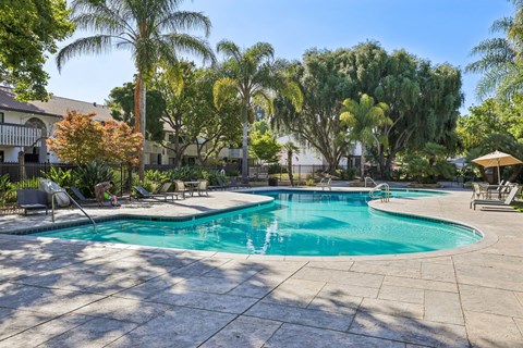 A large outdoor swimming pool surrounded by trees and a patio area with chairs.