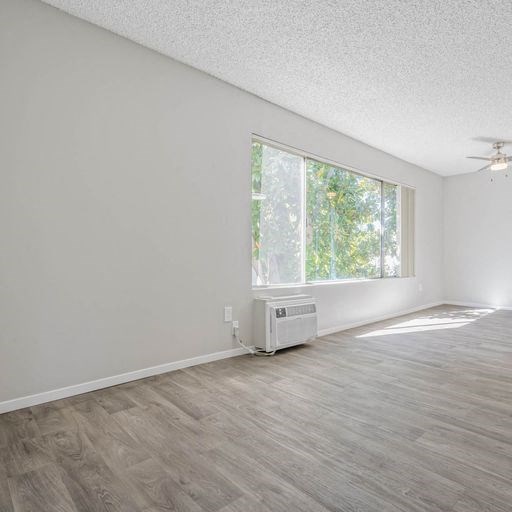 an empty living room with a large window and wooden floors at The Arches Apartments, El Cajon, 92021