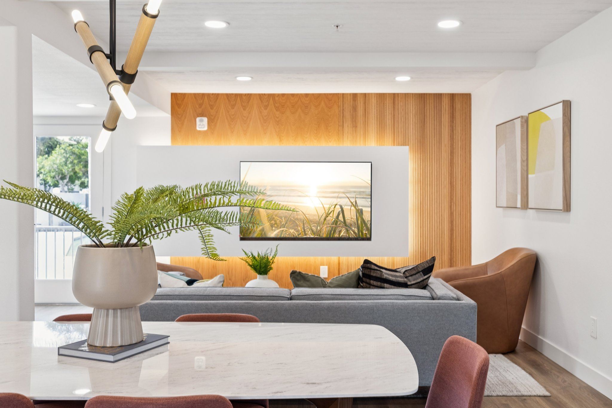 A modern living room with a large painting on the wall and a plant in a white vase on a marble table.