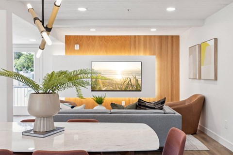 A modern living room with a large painting on the wall and a plant in a white vase on a marble table.