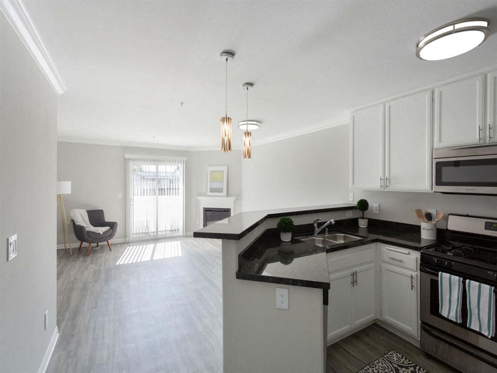 an empty kitchen and living room with white cabinets and black counter tops at Warner Center Townhomes, California, 91303