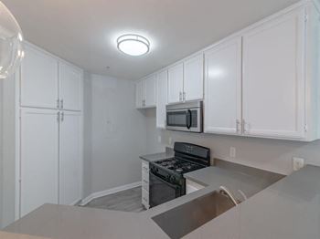 an empty kitchen with white cabinets and a stove and microwave at Warner Center Townhomes, California, 91303
