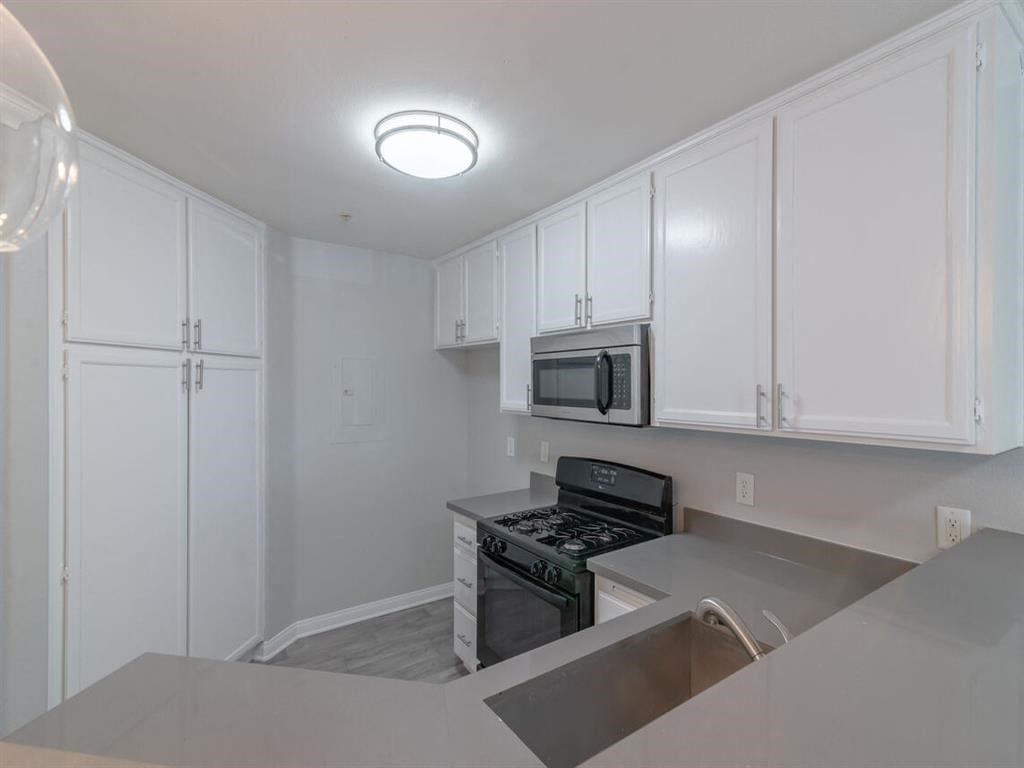 an empty kitchen with white cabinets and a stove and microwave at Warner Center Townhomes, California, 91303