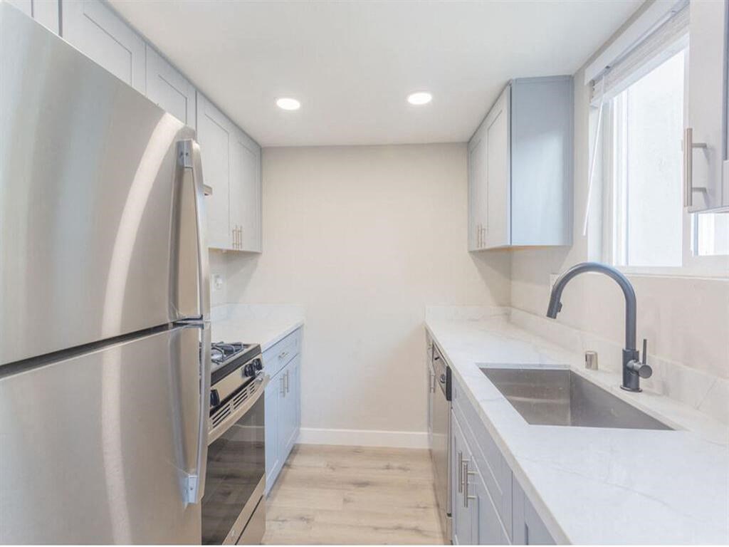 a white kitchen with a stainless steel refrigerator and sink  at The Preston at Hillsdale, San Mateo, CA