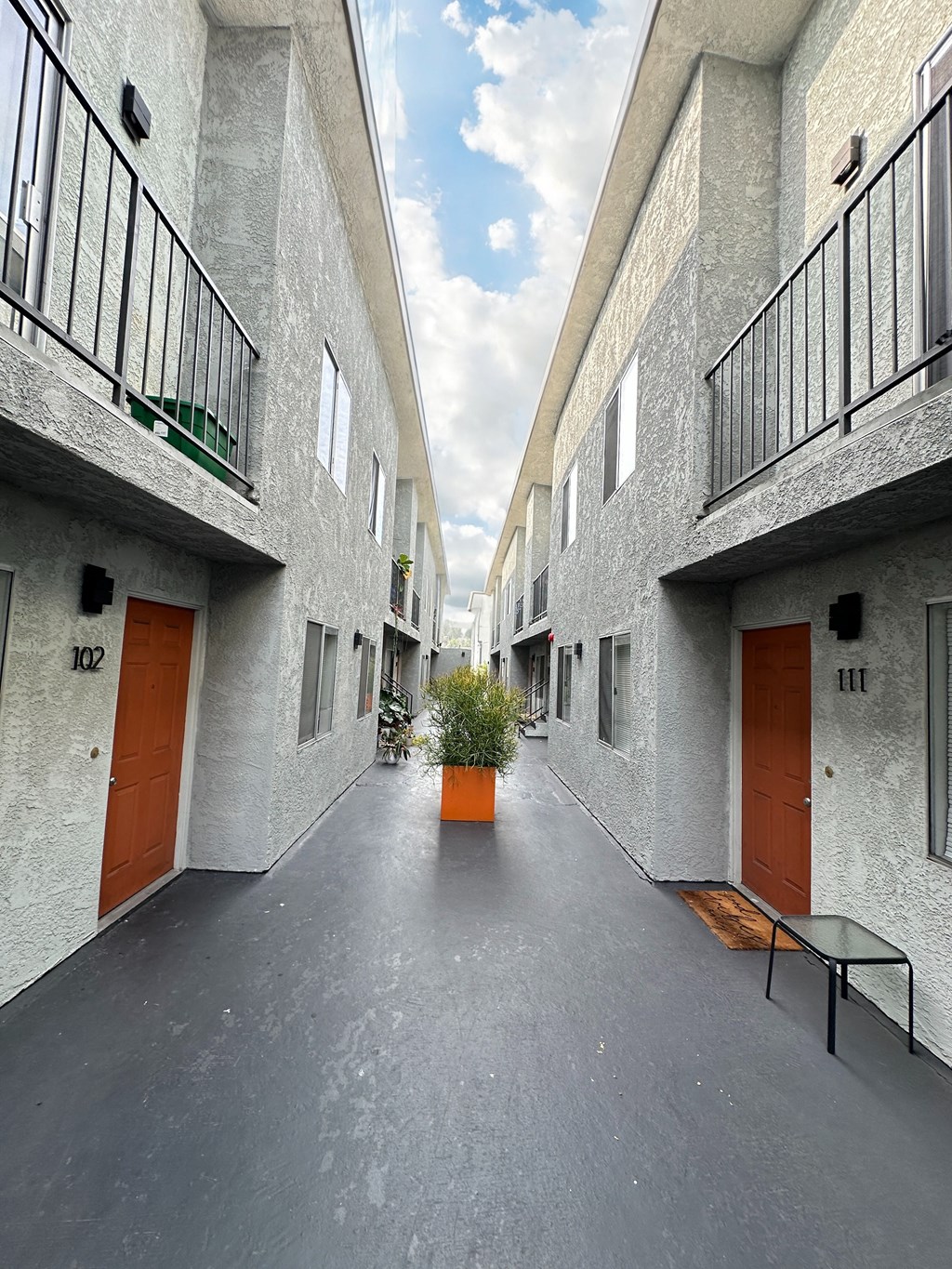 a courtyard between two buildings with orange doors and a potted plant at The Marq Apartments LLC, Los Angeles, California