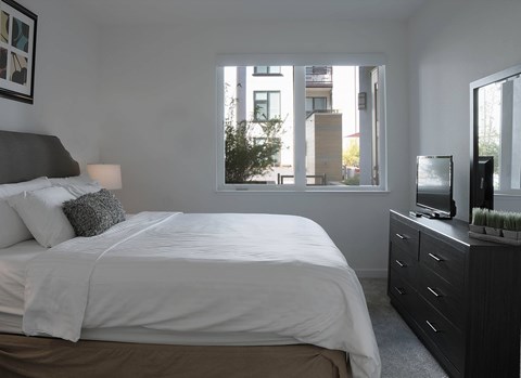 A bedroom with a large bed, a window with a view of a building, and a TV on a dresser at Catalyst Mountain View, Mountain View, CA