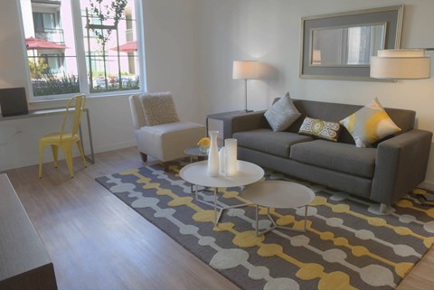 A grey couch with yellow and white pillows sits in a living room with a grey rug and a white coffee table.