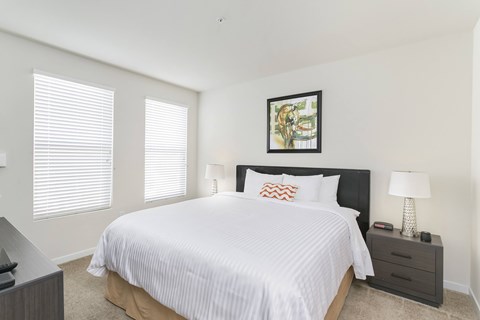 A bedroom with a large bed, a nightstand with a lamp, and a picture on the wall. at Cirrus Redwood City Apartments, Redwood City, CA, 94061