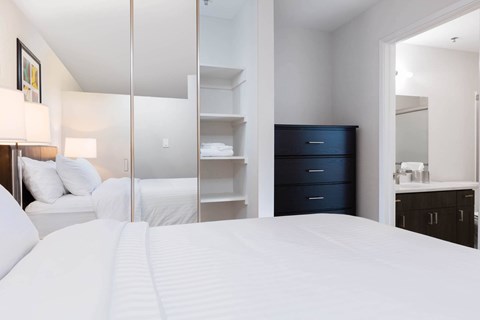A bedroom with a large bed, a dresser, and a mirror. at The Maddox Sunnyvale Apartments, Sunnyvale, 94087