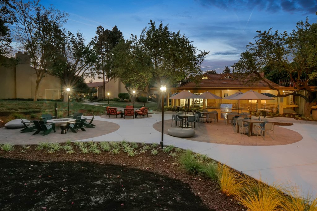 a patio with tables and umbrellas at night at Summerwood Apartments, Santa Clara, CA