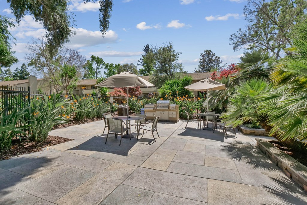 a patio with tables and umbrellas in a garden at Summerwood Apartments, Santa Clara, California