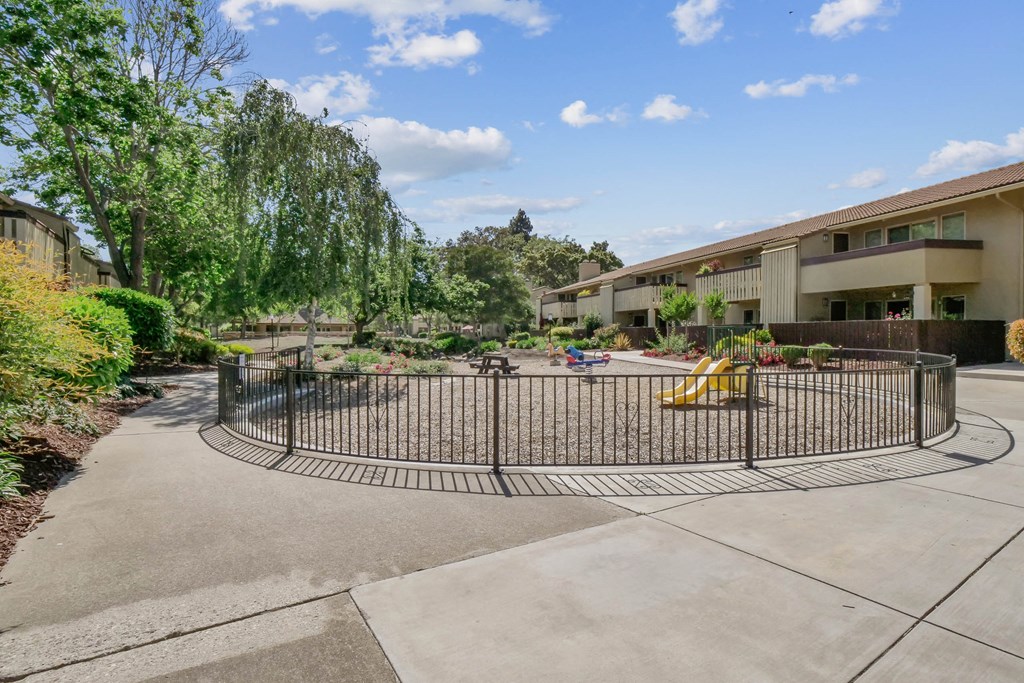 a fenced in play area with a playground in front of a building at Summerwood Apartments, Santa Clara, California