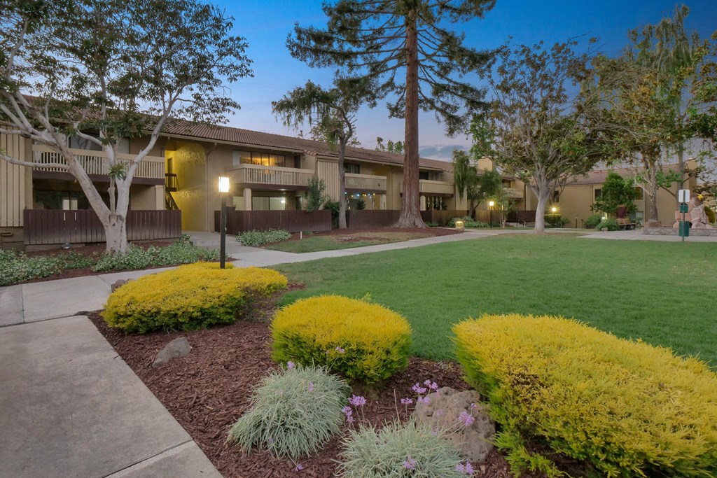 an exterior view of a building with green grass and trees at Summerwood Apartments, Santa Clara, California
