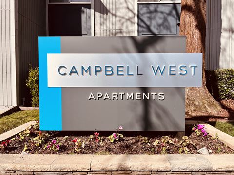a sign for the campbell west apartments in front of a garden
