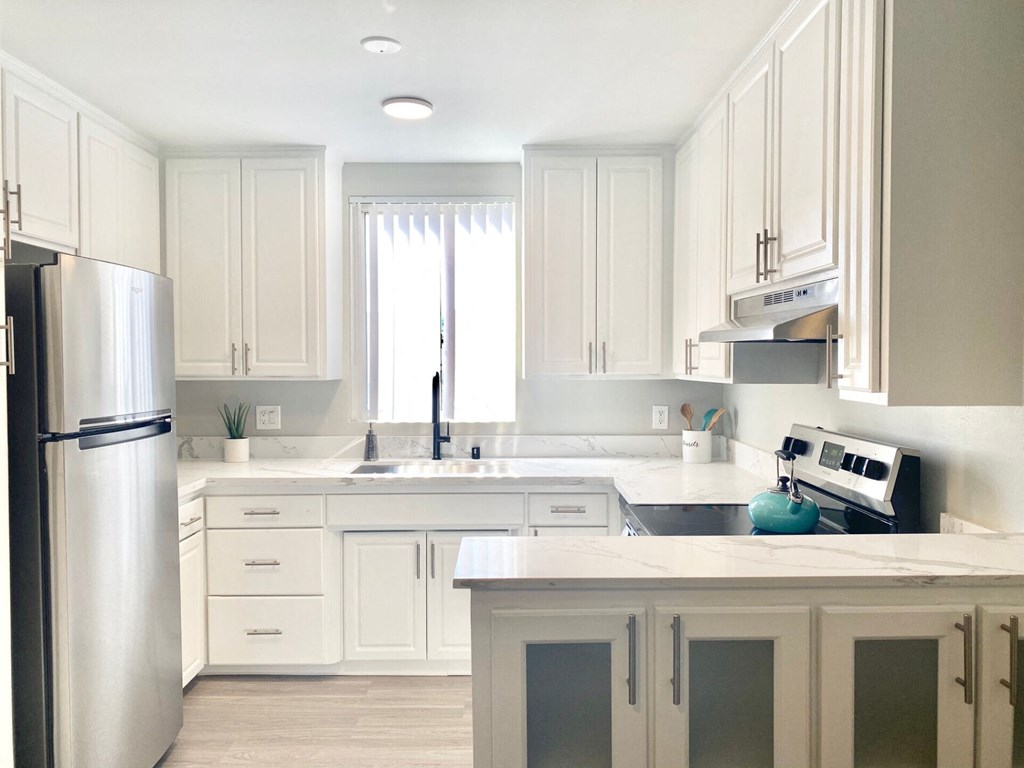 a white kitchen with white cabinets and a stainless steel refrigerator at The Flats on Addison, California