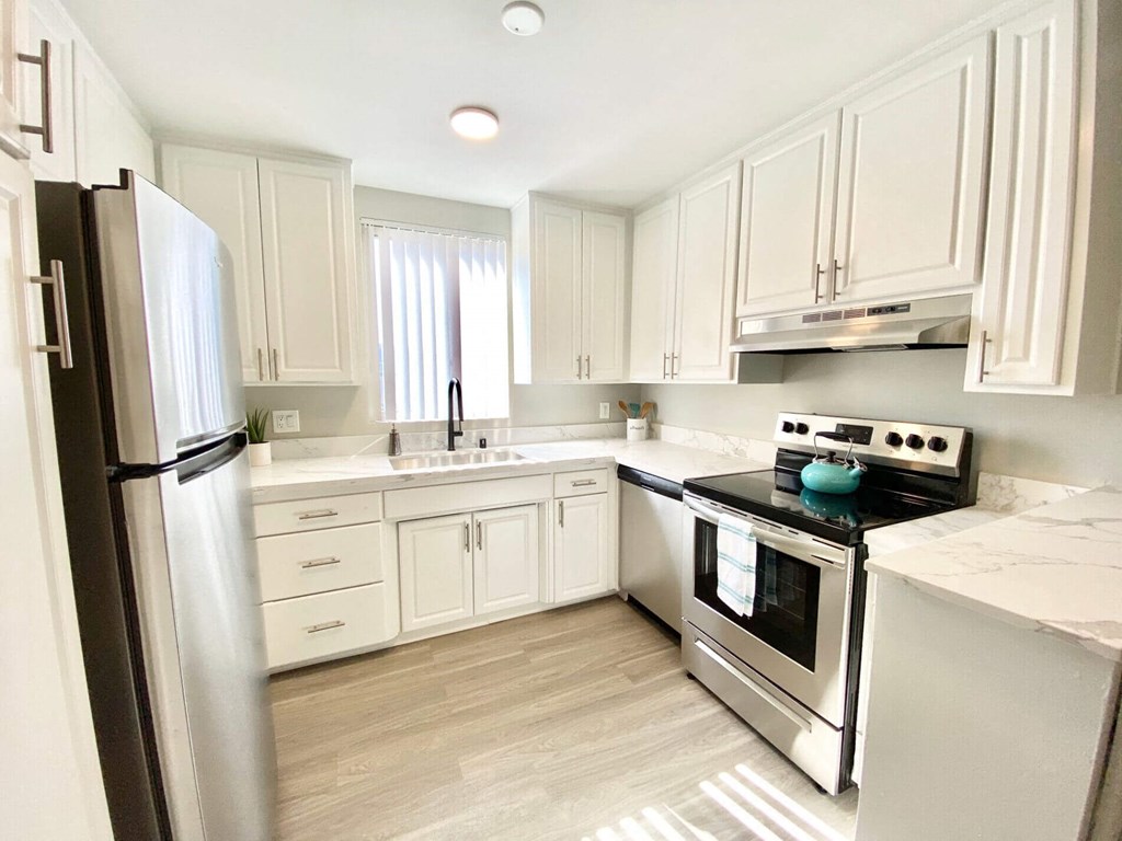 a white kitchen with stainless steel appliances and white cabinets at The Flats on Addison, Sherman Oaks, CA 91423
