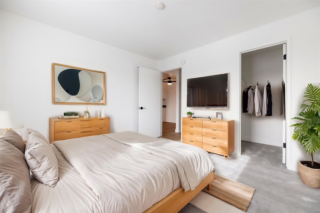 A bedroom with a bed, nightstand, and a plant.