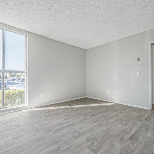 an empty living room with a large window and wooden floors at The Arches Apartments, California, 92021