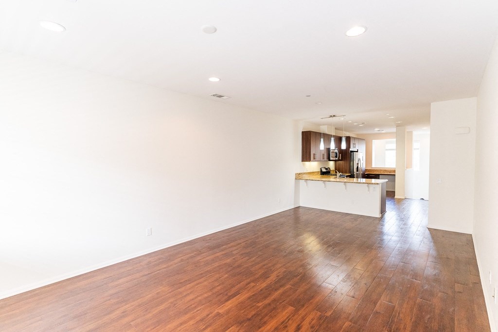 an empty living room and kitchen with wood floors and white walls at The Vines at Riverpark, LLC, California, 93036