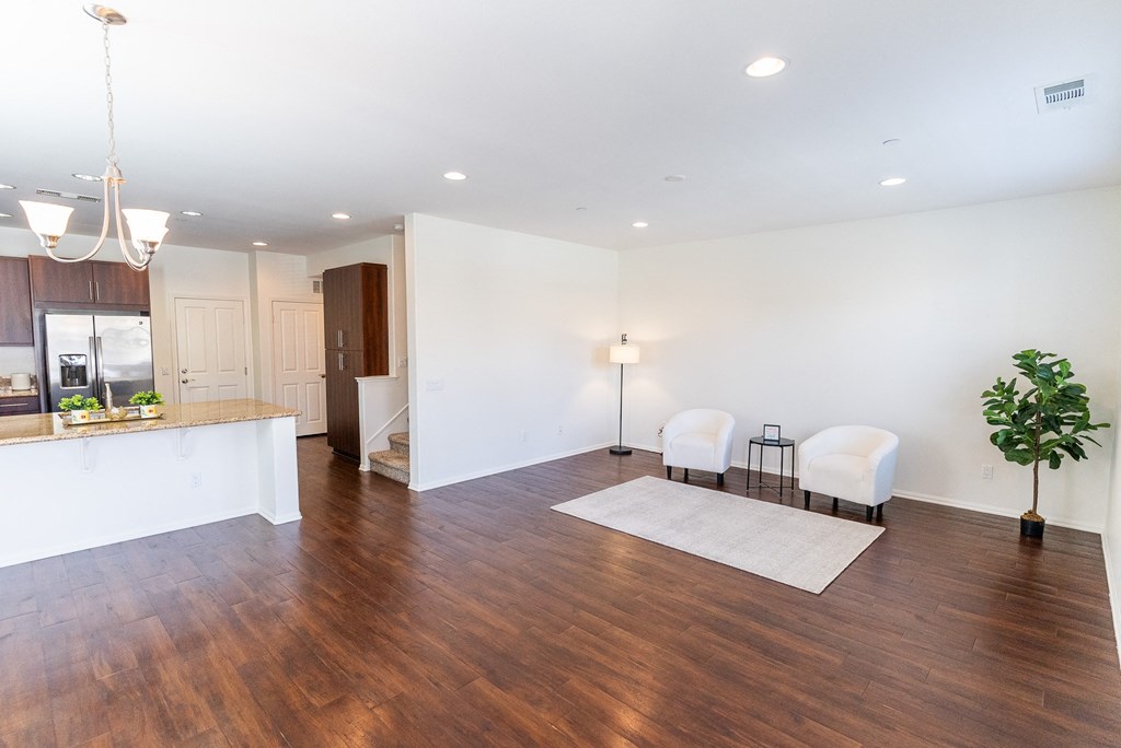 an empty living room and kitchen with hard wood flooring and white walls at The Vines at Riverpark, LLC, California, 93036