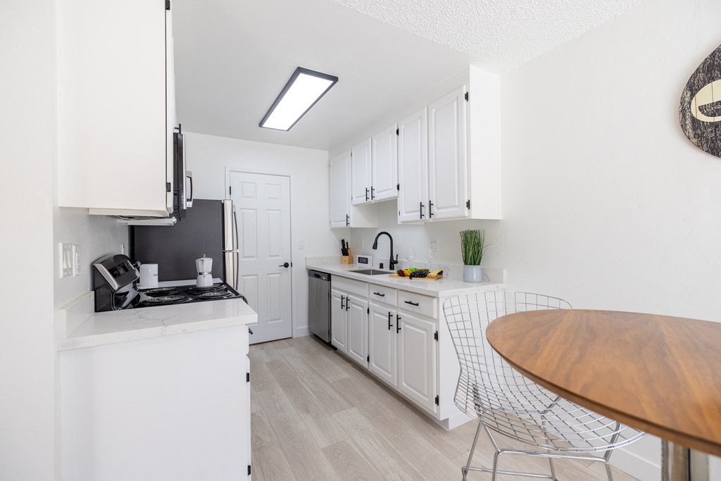 a white kitchen with white cabinets and a wooden table and counter top at Campbell West Apartments, Campbell, CA