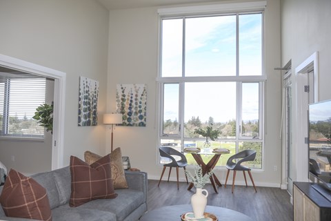 A living room with a grey couch and a large window.at 888 Fourth Street Apartments, LLC, Santa Rosa California
