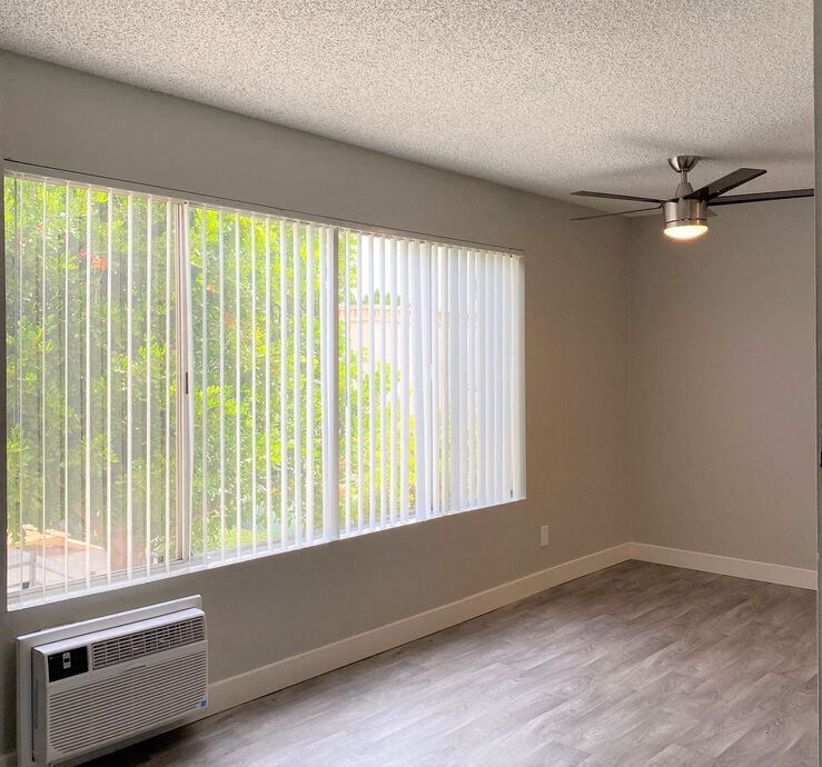 an empty living room with a large window and a ceiling fanat The Arches Apartments, LLC, El Cajon