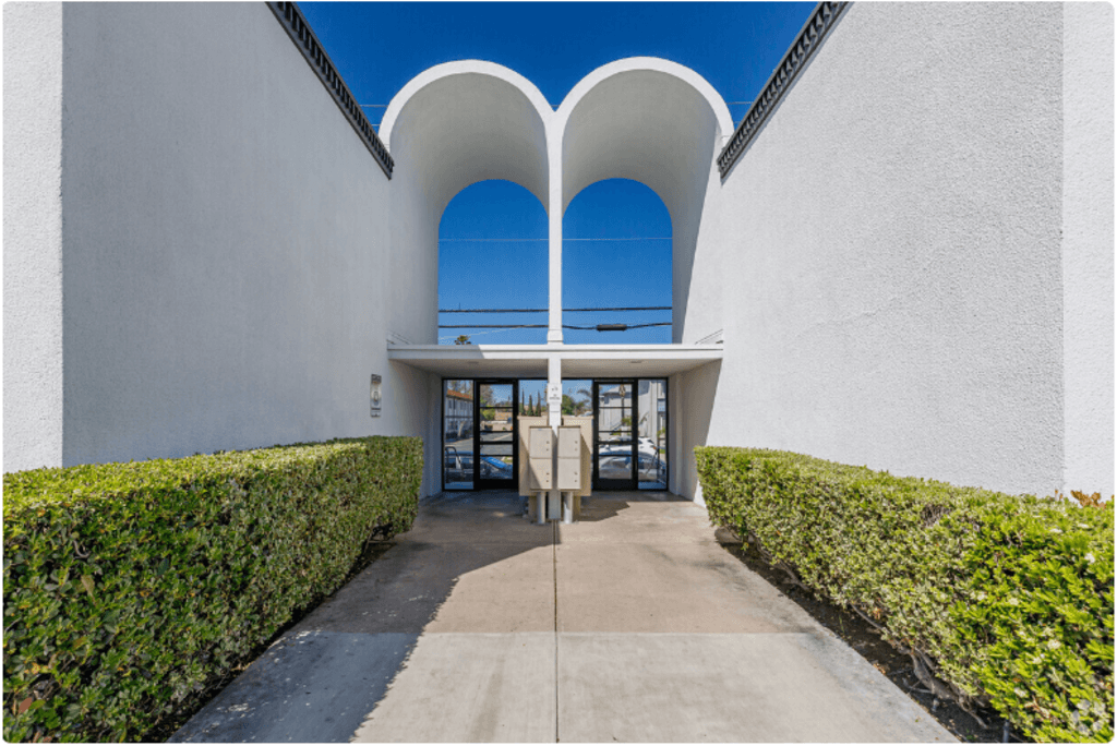 a walkway leading to the entrance of a white building with blue skiesat The Arches Apartments, LLC, El Cajon, CA