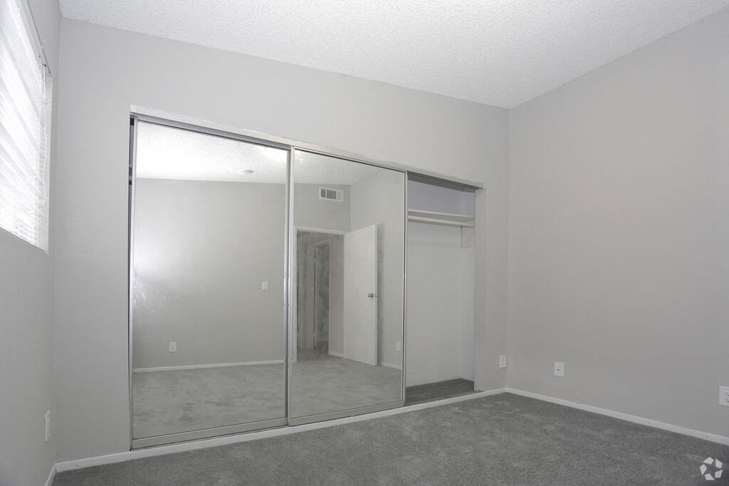 an empty living room with a large window and a mirrored closet  at The Marq Apartments LLC, Los Angeles, California