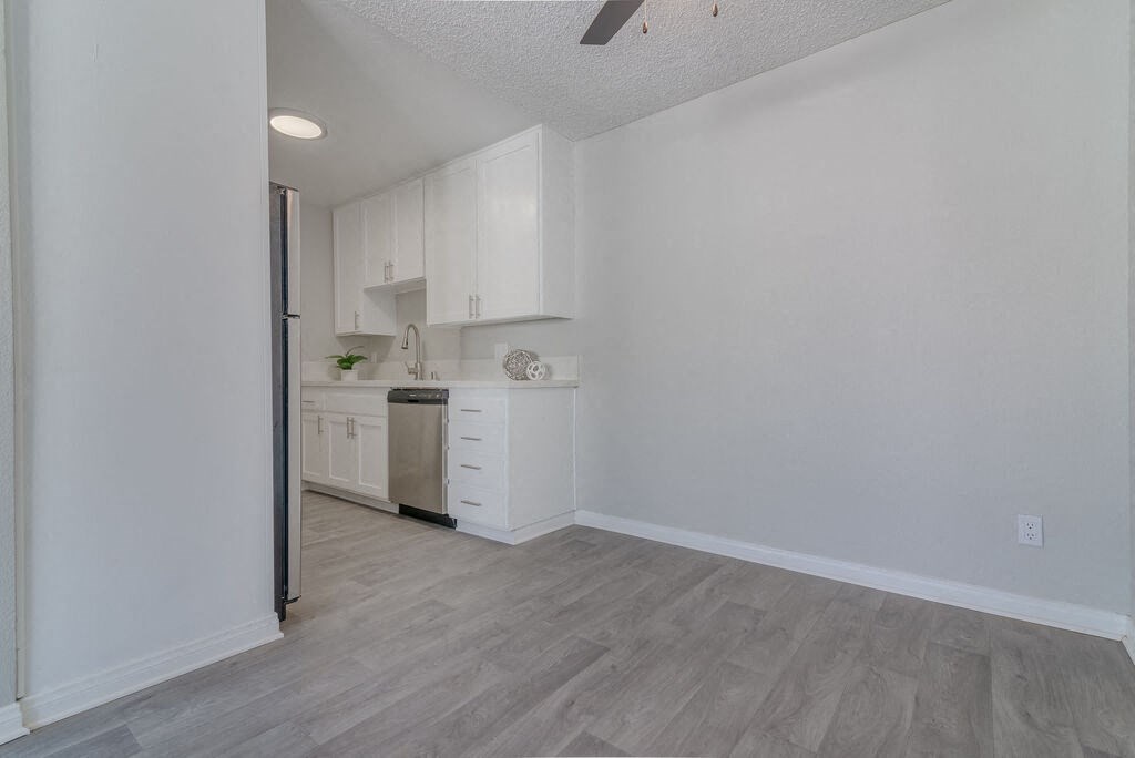 an empty kitchen with white cabinets and white walls and wood floors at Citra Apartments LLC, San Diego, 92107