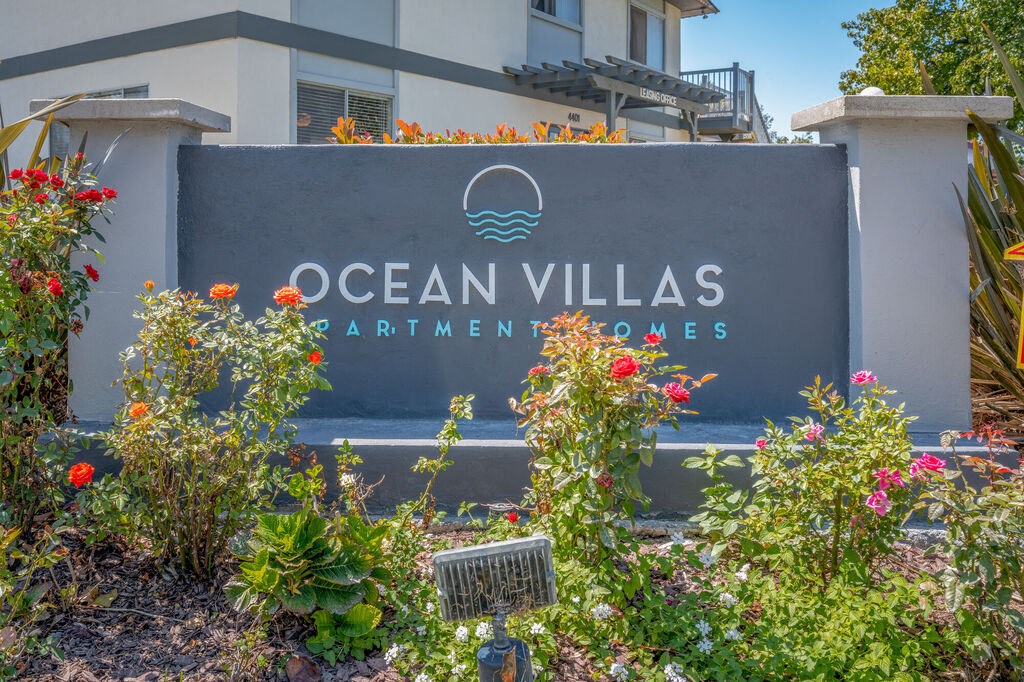 a sign for ocean villas apartments with flowers in front of it at Ocean Villas, Oxnard, CA 93033