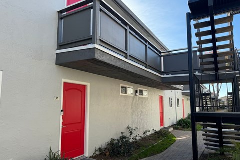 A white building with a red door and a balcony with a black railing.