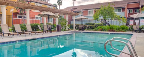 A pool with a metal ladder and a few chairs and umbrellas.