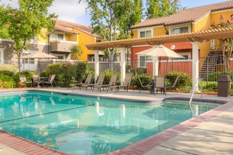 A pool surrounded by chairs and umbrellas with a building in the background.