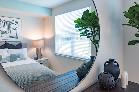 A bedroom with a round mirror and a bed with a grey blanket.
