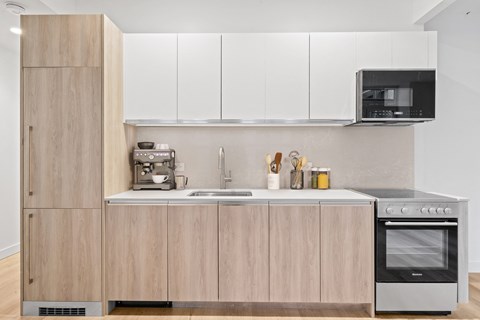 Modern kitchen with wood grain cabinetry at ARIA 90-100 John Apartments, New York, NY 10038