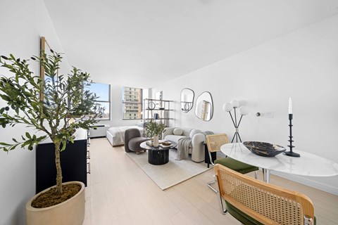 A living room with a tree in a pot, a white table, and a chair at One West, New York, New York.