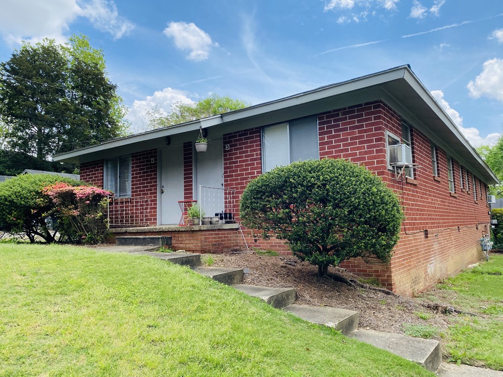 the front of a brick house with a porch and a lawn