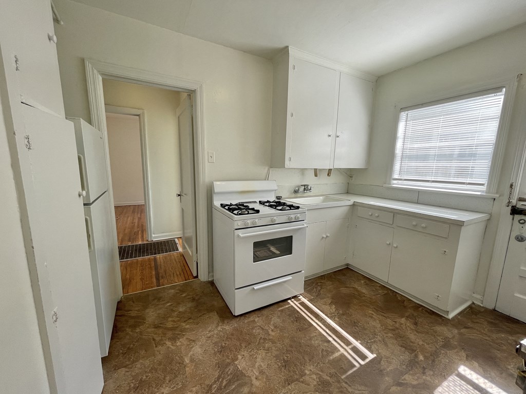 an empty kitchen with white cabinets and a stove and a window
