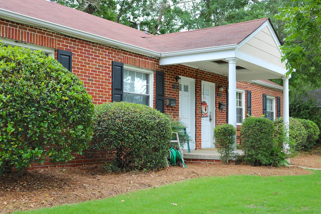 the front of a brick house with a porch and a lawn