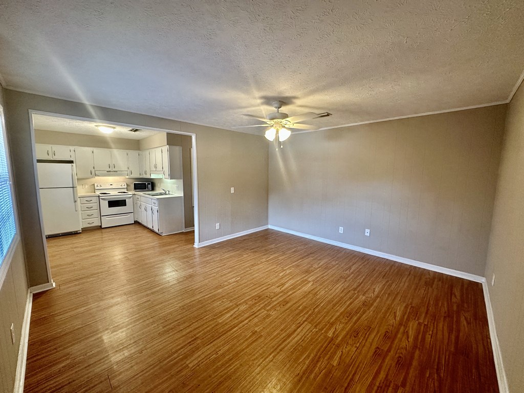 an empty living room and kitchen with wood floors and a ceiling fan