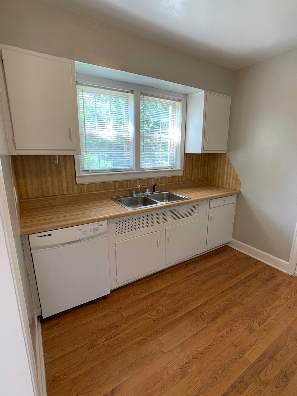 an empty kitchen with wooden floors and white cabinets