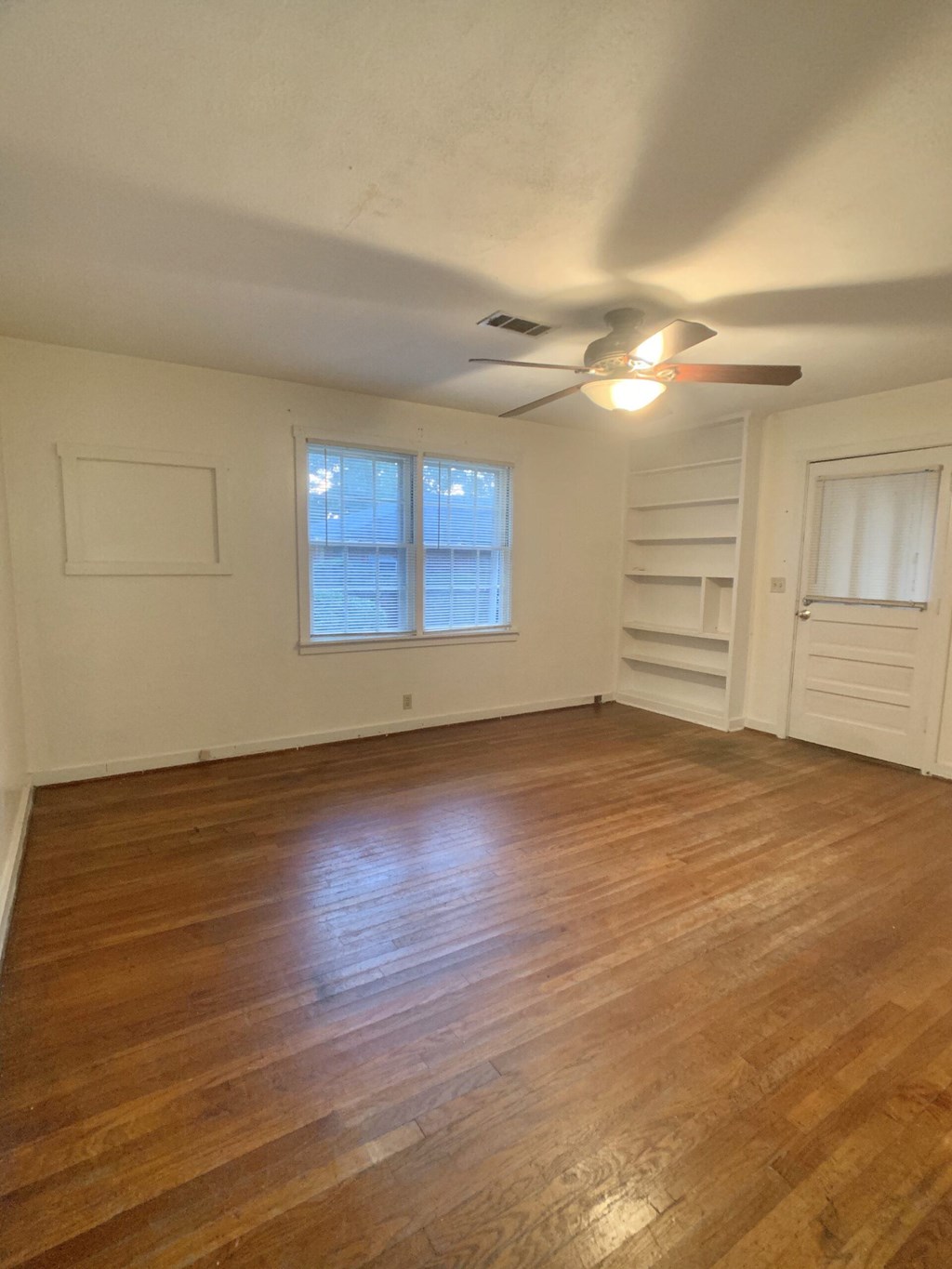 an empty living room with wooden floors and a ceiling fan