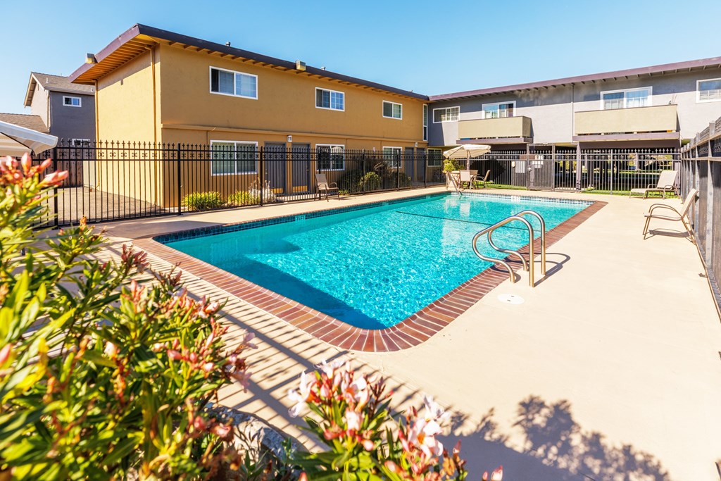 A pool surrounded by a black fence and a yellow building.