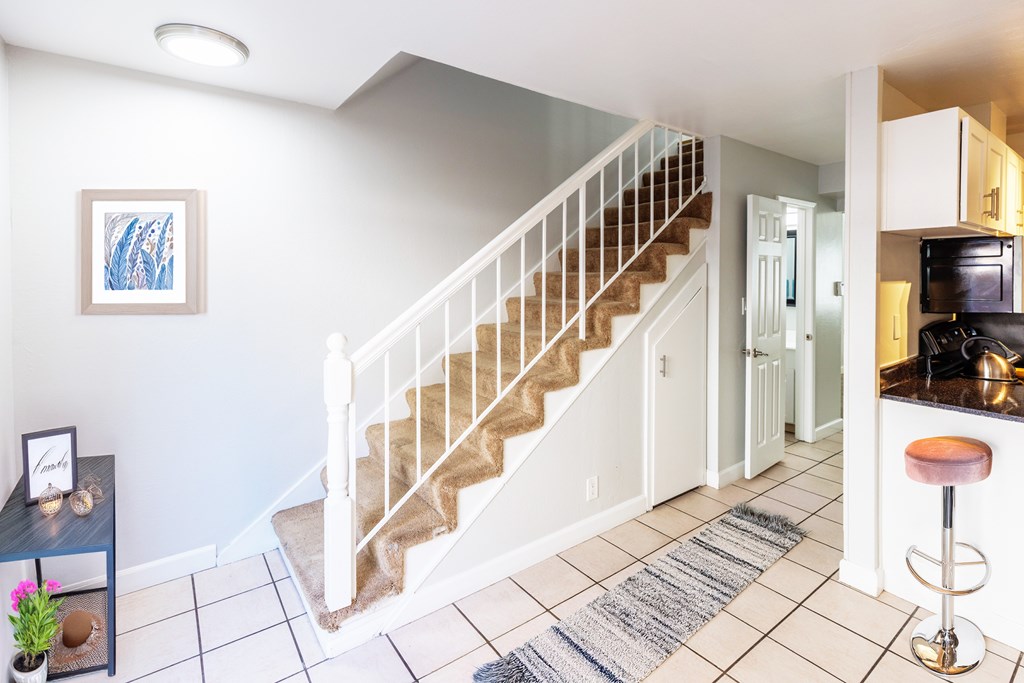 A staircase with a white railing and beige carpeted steps leads to a kitchen area.