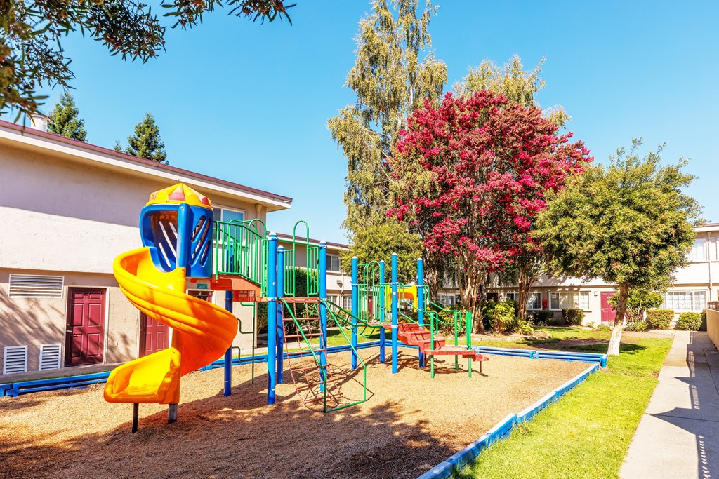 A playground with a yellow slide and a red bench.