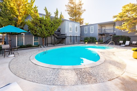 A round swimming pool surrounded by a concrete patio and a building in the background.